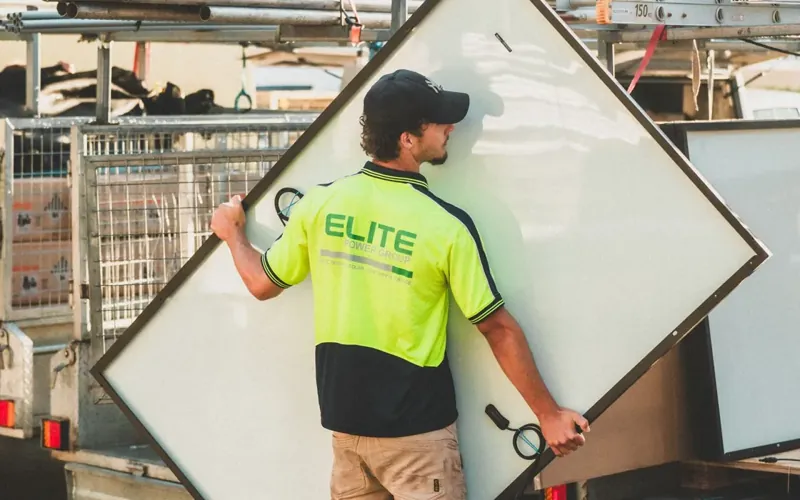 Tradie in hi-vis carrying a solar panel to his ute