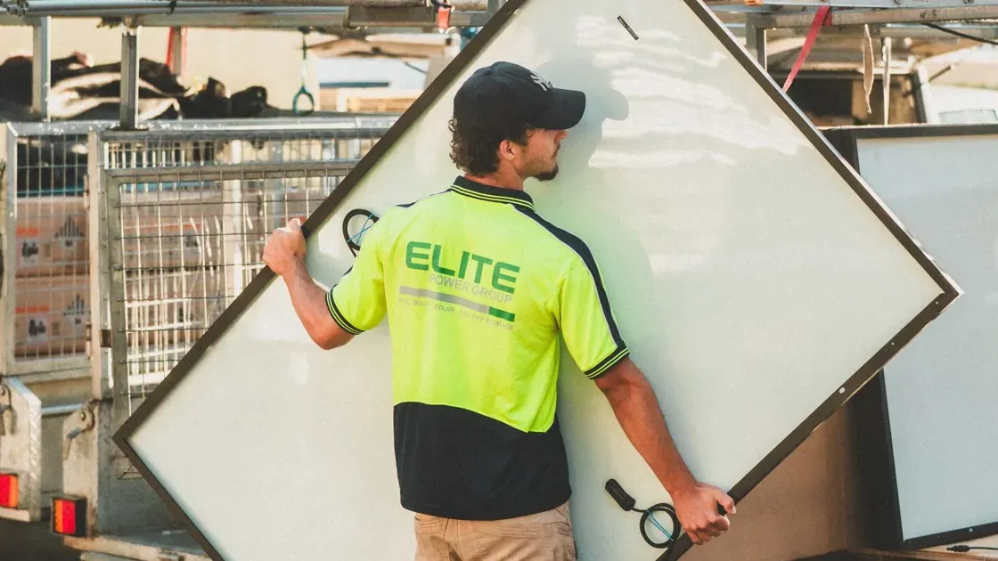 Tradie in hi-vis carrying a solar panel to his ute